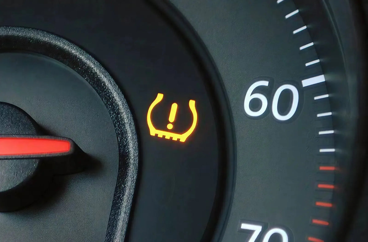 Muestra a un automovilista al aire libre en una estación de servicio utilizando una manguera de aire comprimido para inflar el neumático de un coche, montado en una llanta de aleación personalizada.