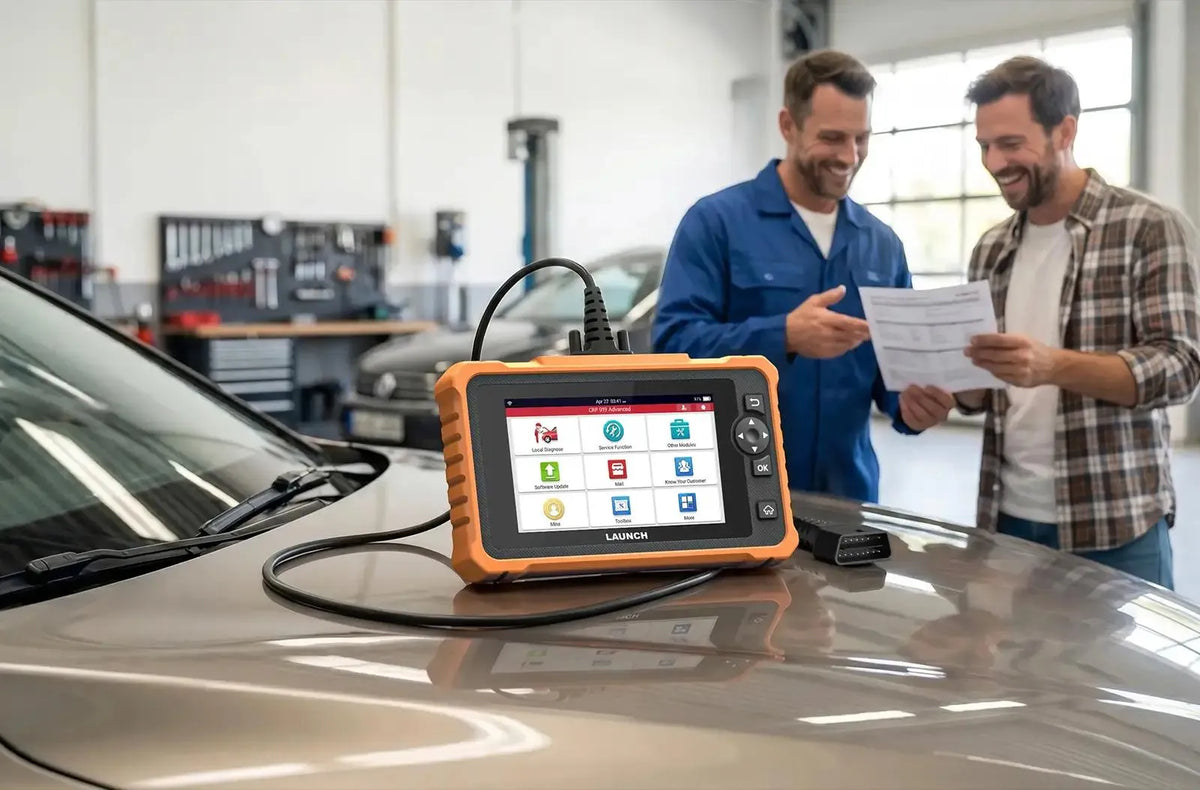 Una herramienta de diagnóstico LAUNCH CRP 919 Advanced apoyada sobre el capó de un automóvil dentro de un taller mecánico. Al fondo, un mecánico con mono azul y un cliente sonríen mientras revisan juntos un informe de diagnóstico impreso.
