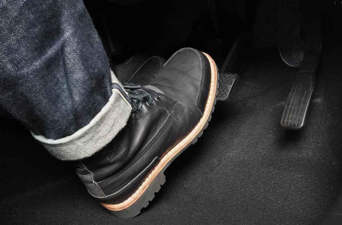 Primer plano de una bota de cuero negro pisando con fuerza el pedal de freno.