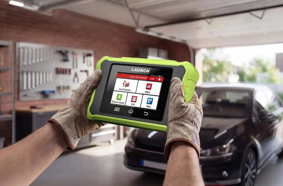 Una persona con guantes de trabajo sostiene una herramienta de diagnóstico LAUNCH Creader Elite X500 BM. El dispositivo tiene una funda protectora verde brillante y su pantalla táctil muestra íconos del menú como «Diagnóstico local» y «OBD II».