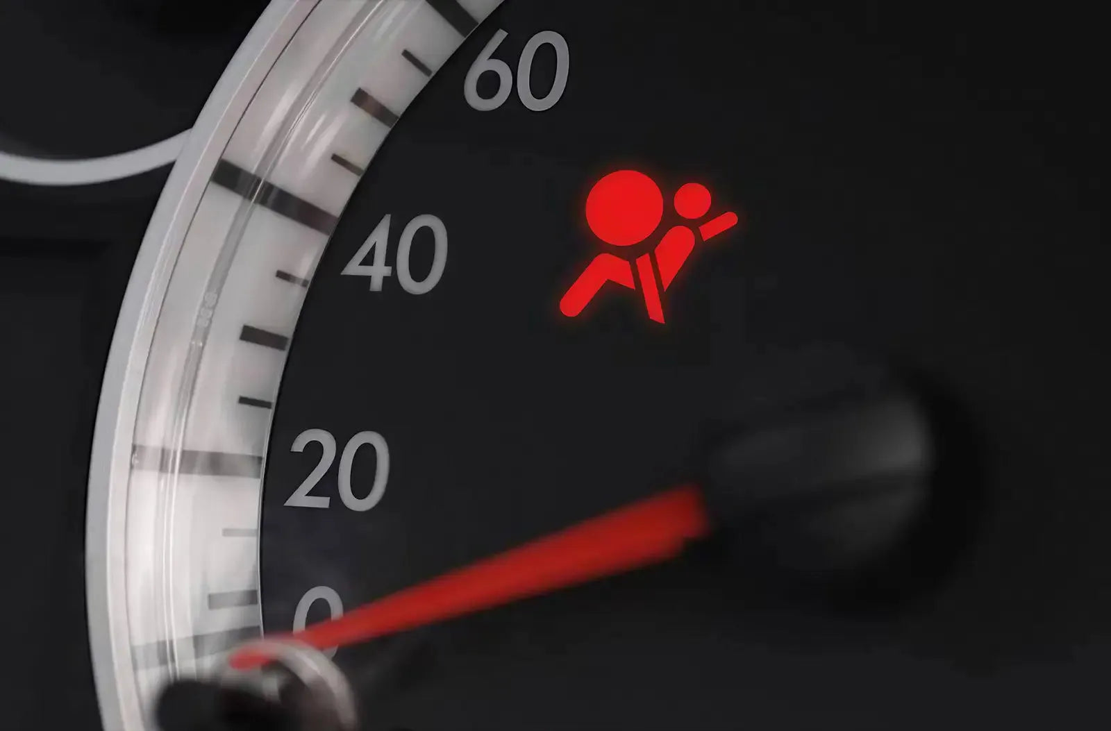 Primer plano del cuadro de instrumentos analógico de un vehículo, con el testigo rojo de seguridad del airbag/SRS prominentemente iluminado.
