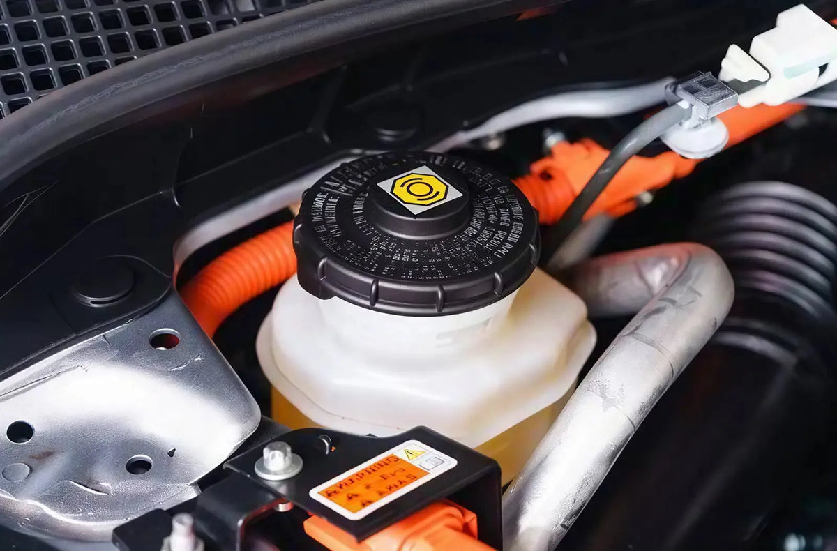 Muestra a un mecánico trabajando en un taller, utilizando una llave larga para abrir la válvula de purga de la pinza de freno detrás del conjunto del disco de freno metálico de un coche.