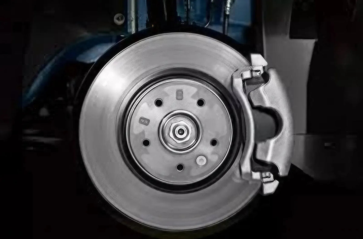 Primer plano desde el espacio reposapiés del conductor con una bota de cuero negra presionando con fuerza el pedal de freno de goma del vehículo.