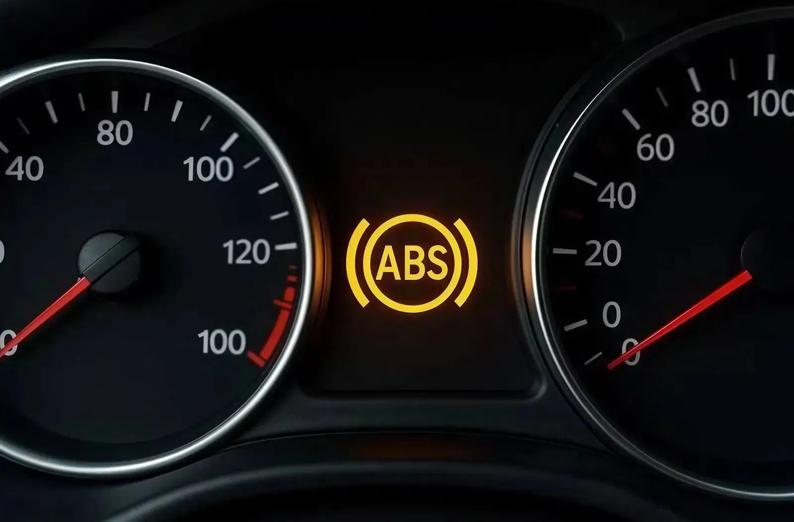 Muestra la perspectiva del conductor desde detrás del volante de noche en una carretera mojada, destacando el testigo amarillo del "ABS" iluminado en la pantalla central del cuadro de instrumentos.