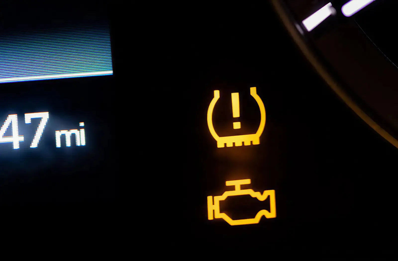 Vista tras el volante que muestra el testigo amarillo de «Baja presión de neumáticos / TPMS» con signo de exclamación iluminado en el centro del cuadro de instrumentos.