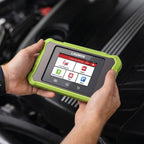 Una persona sosteniendo una herramienta de diagnóstico LAUNCH Creader Elite X500 BM sobre el compartimento del motor de un coche. El dispositivo cuenta con una resistente protección verde lima y una pantalla táctil que muestra opciones de menú como Diagnóstico local, OBD II y Actualización de software.